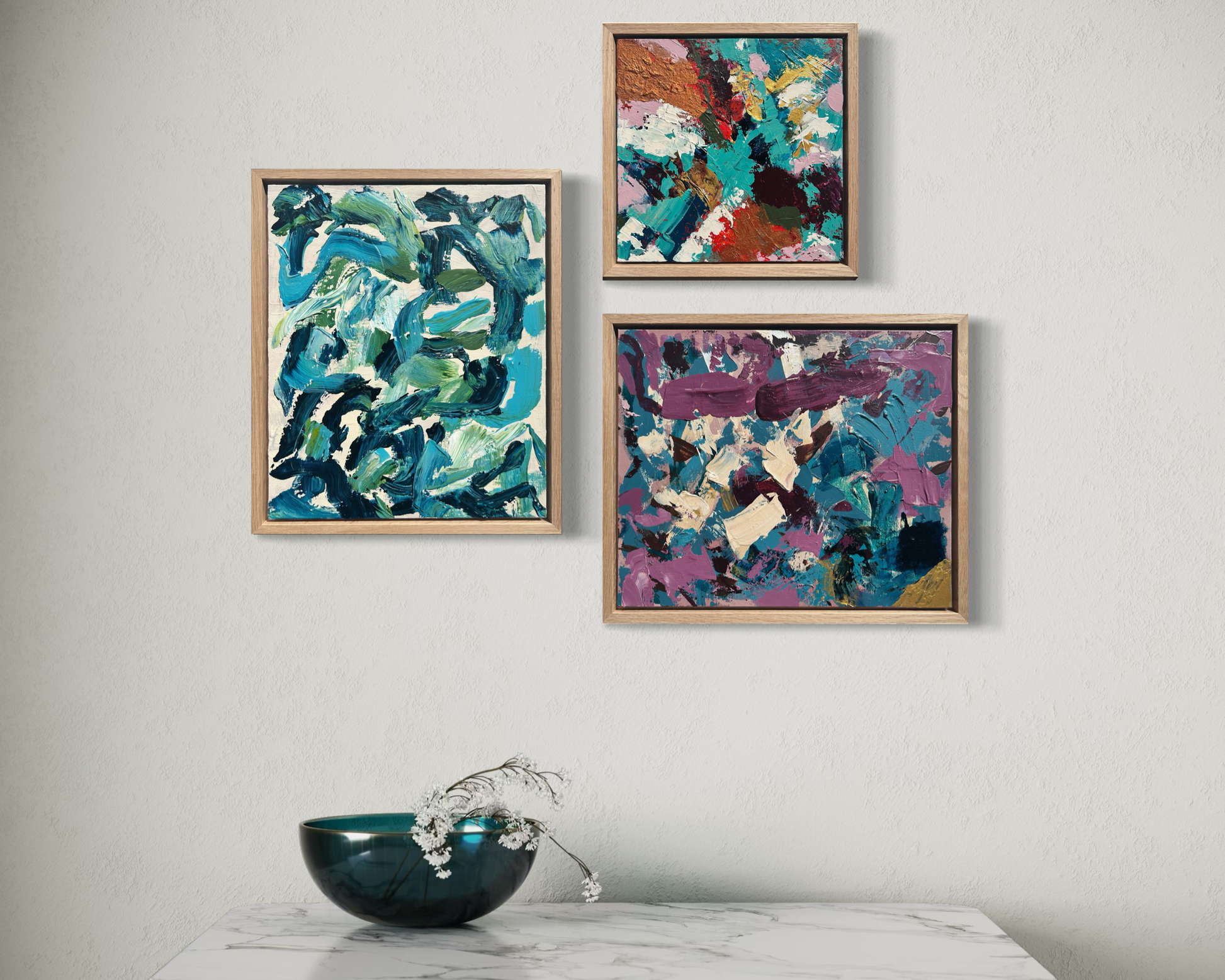 Three abstract paintings on a wall above a marble table with a decorative bowl.
